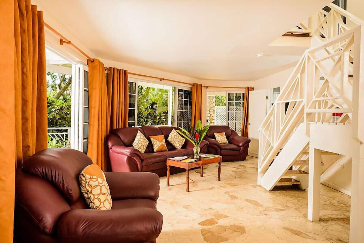 A spacious living area with a brown leather sofa set, a coffee table, and a staircase with a white railing.