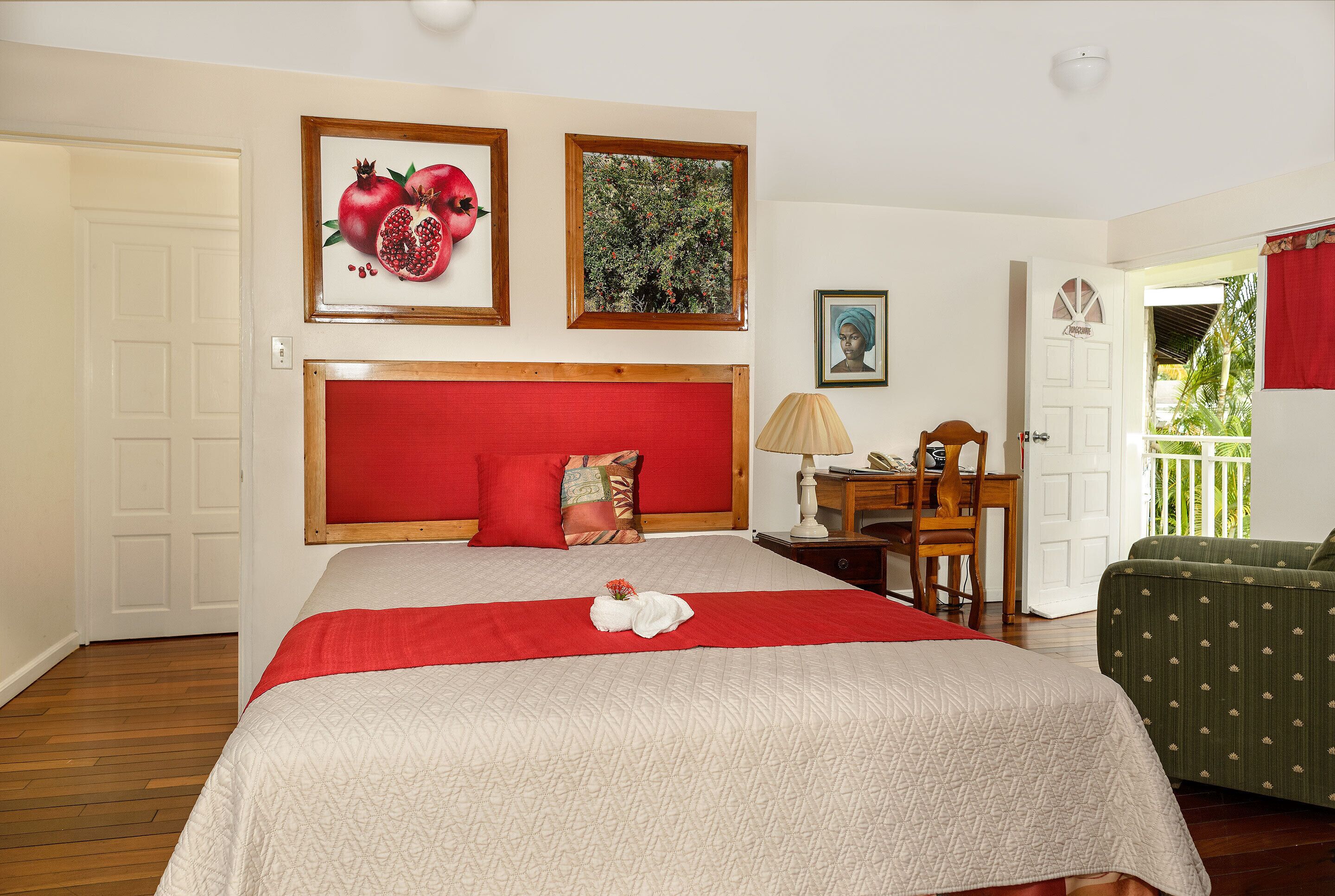 A hotel room with a large bed, a red headboard, a wooden nightstand, a green armchair, and a window with a view of greenery.