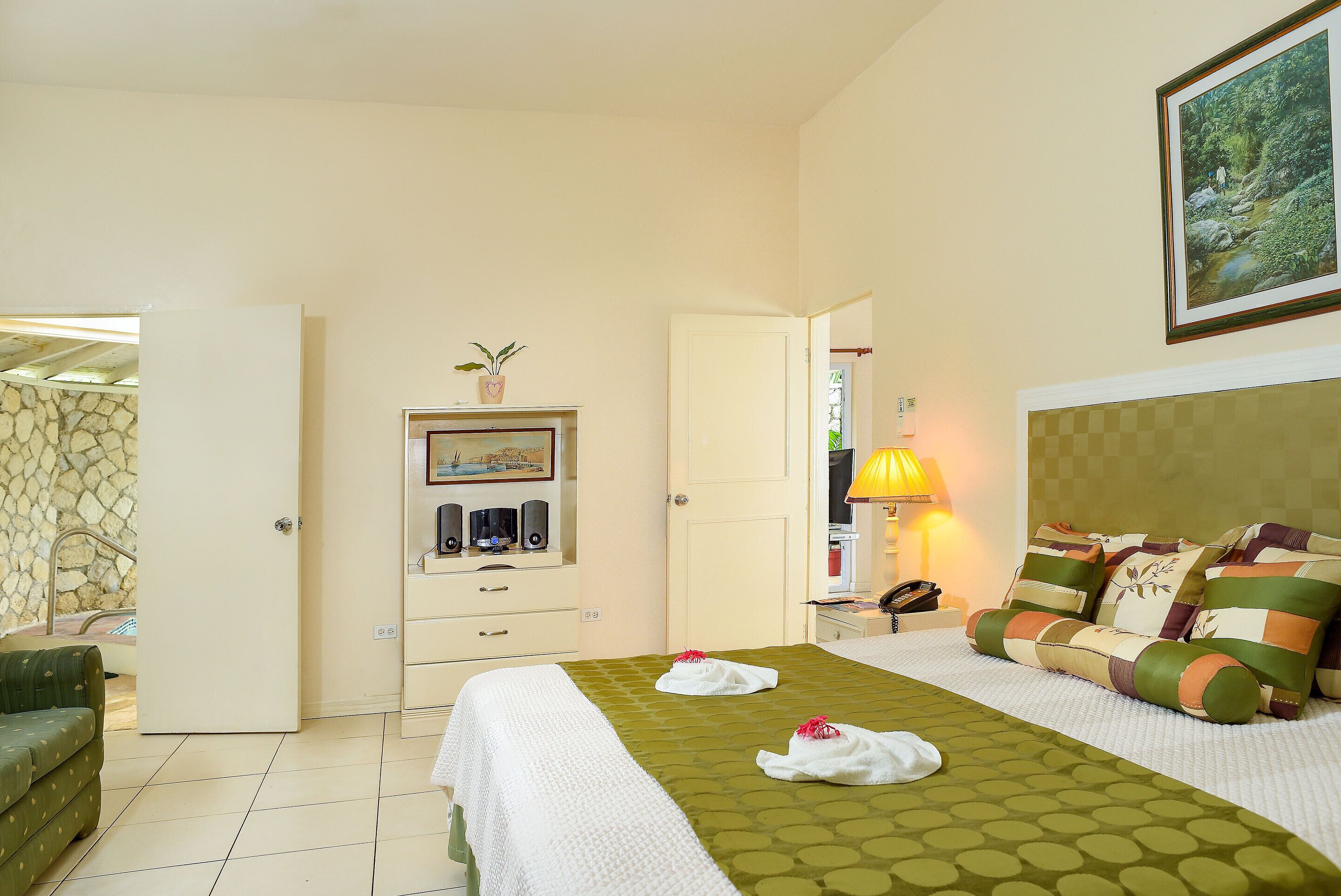 A hotel room with a bed, a desk, a lamp, and a painting on the wall.