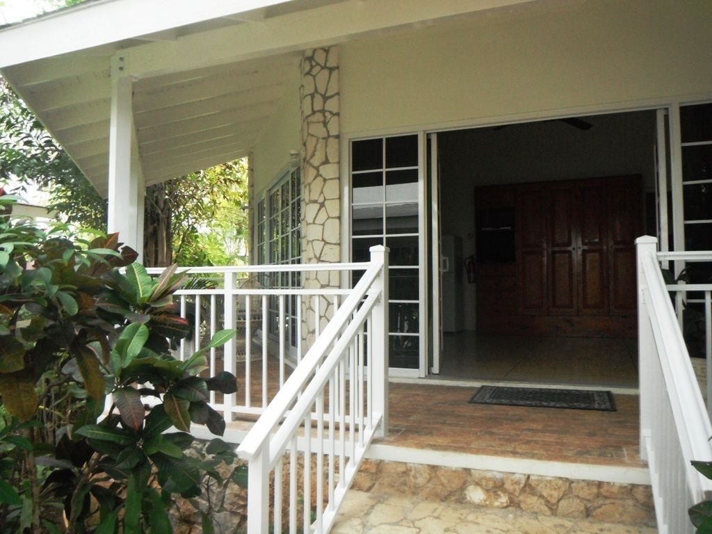 A covered porch with a stone column, a white railing, and a view into a room with wooden cabinets.