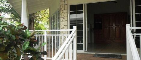 A covered porch with a stone column, a white railing, and a view into a room with wooden cabinets.