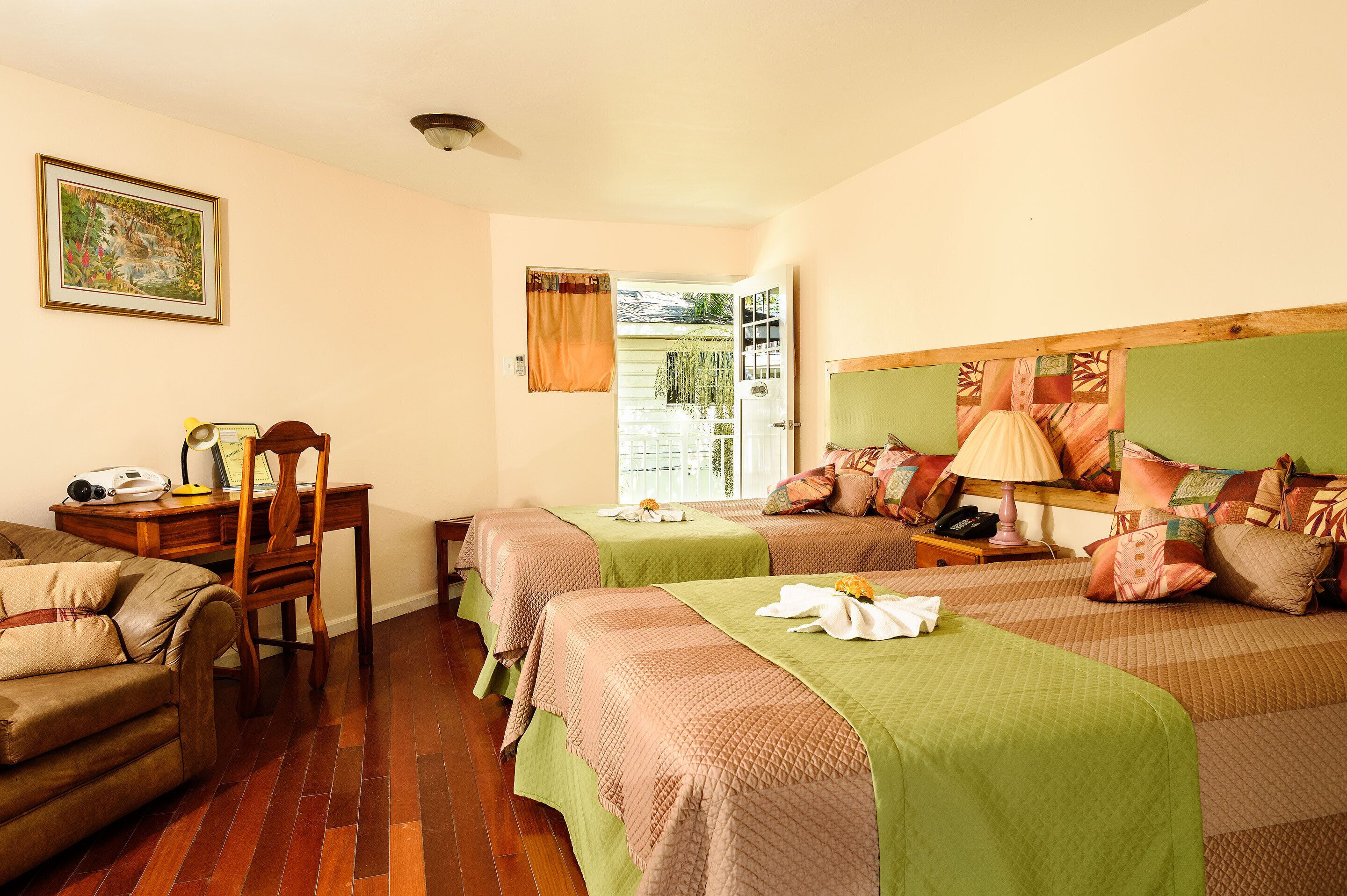 Habitación de hotel con dos camas, un escritorio, una silla y un ventanal con cortinas.