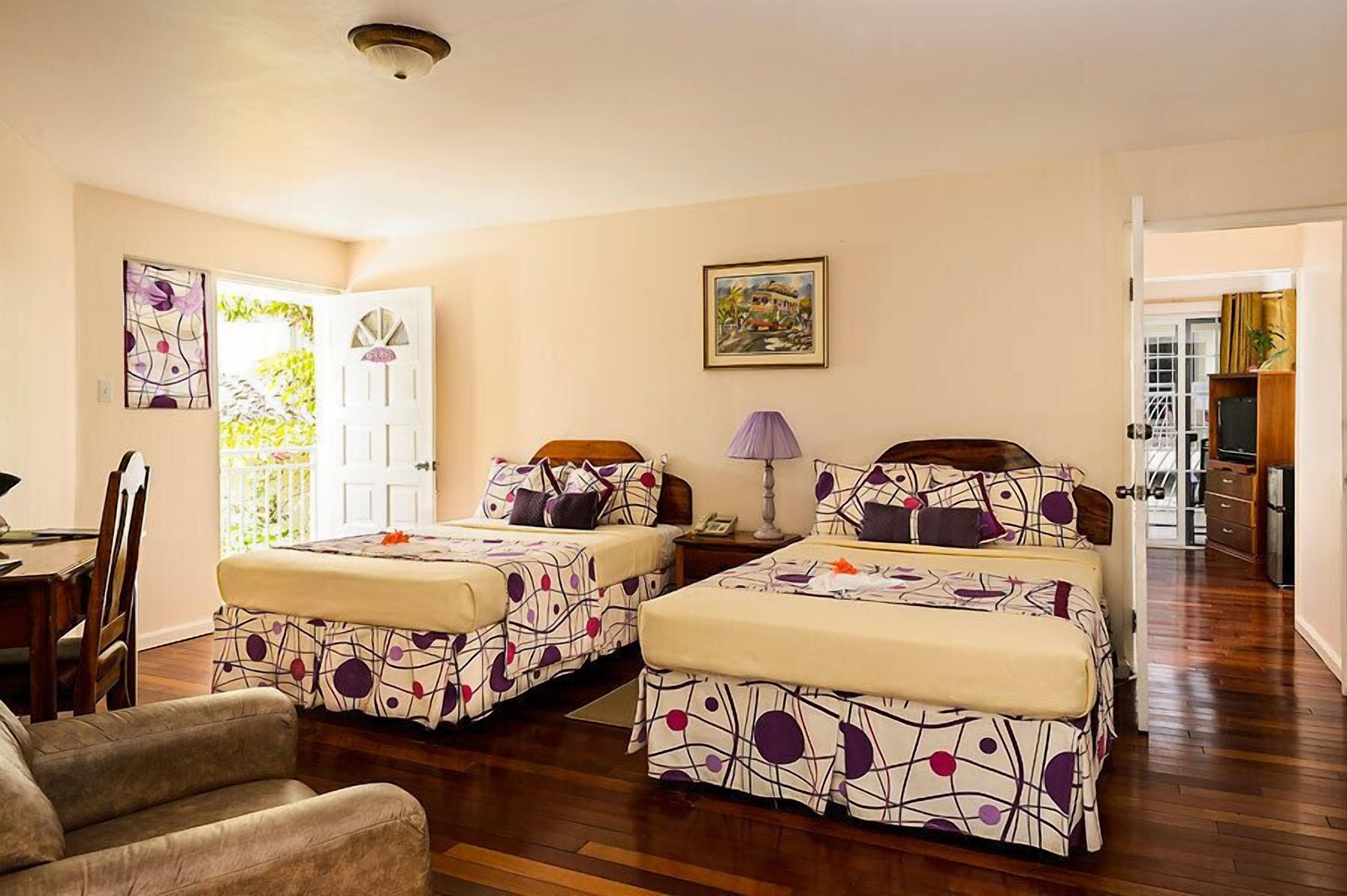 Una habitación de hotel con dos camas, un escritorio, una silla, una lámpara y un cuadro en la pared.