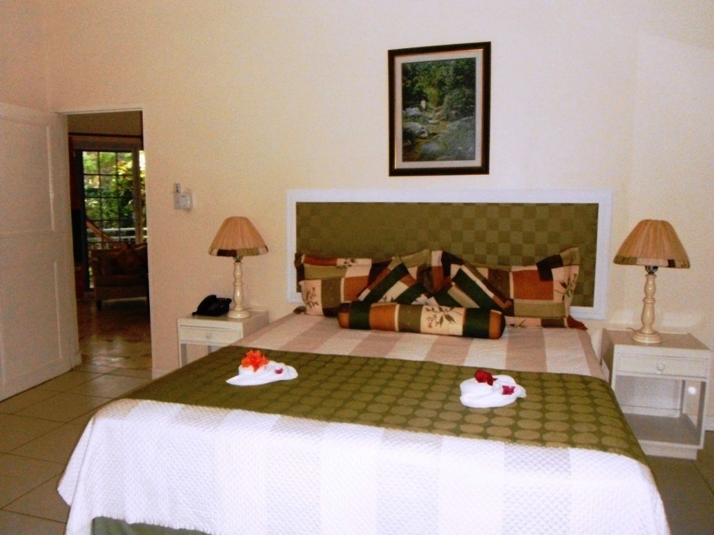 A hotel room with a bed, two bedside tables, a nightstand, a framed picture on the wall, and a door leading to another room.