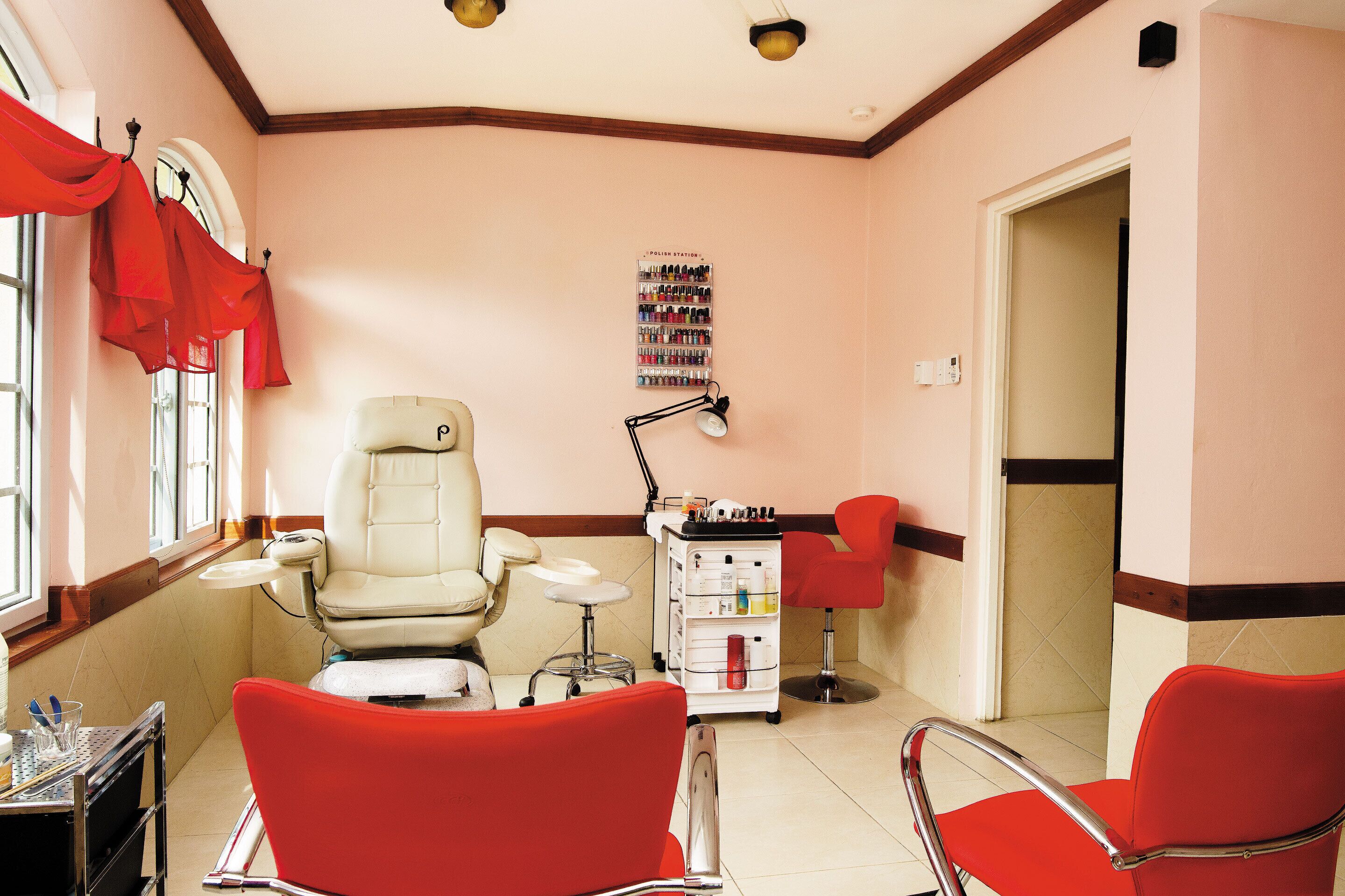 A salon with two red chairs, a white salon chair, a nail polish wall, and a small cart with supplies.