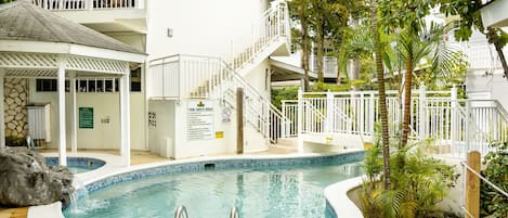 A swimming pool with a white fence, a covered area, and a two-story building with balconies.