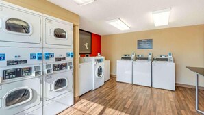 Une buanderie équipée de plusieurs machines à laver et de plusieurs sèche-linge, dotée d’un plancher en bois et d’un mur d’accent de couleur rouge.