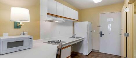 A compact kitchen with white cabinets, a microwave, a refrigerator, and a sink.