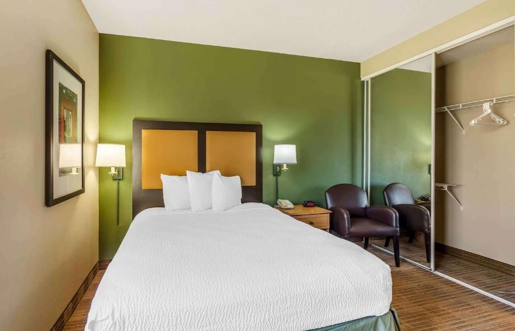 Une chambre d’hôtel avec un grand lit, deux chaises, un bureau avec une lampe et un miroir.