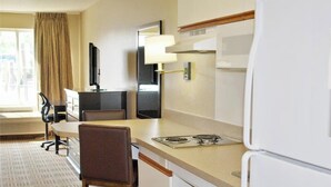 Une chambre d’hôtel compacte comprenant un coin cuisine, un espace repas, une télévision et une fenêtre avec des rideaux.