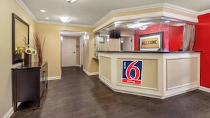Un hall d'hôtel avec une enseigne indiquant « 6 suites », une autre enseigne avec le mot « BIENVENUE », un plancher en bois foncé, un miroir et un vase contenant des branches séchées.