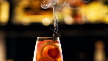 Een cocktailglas met garnering, damp die opstijgt, en een onscherpe achtergrond van flessen.