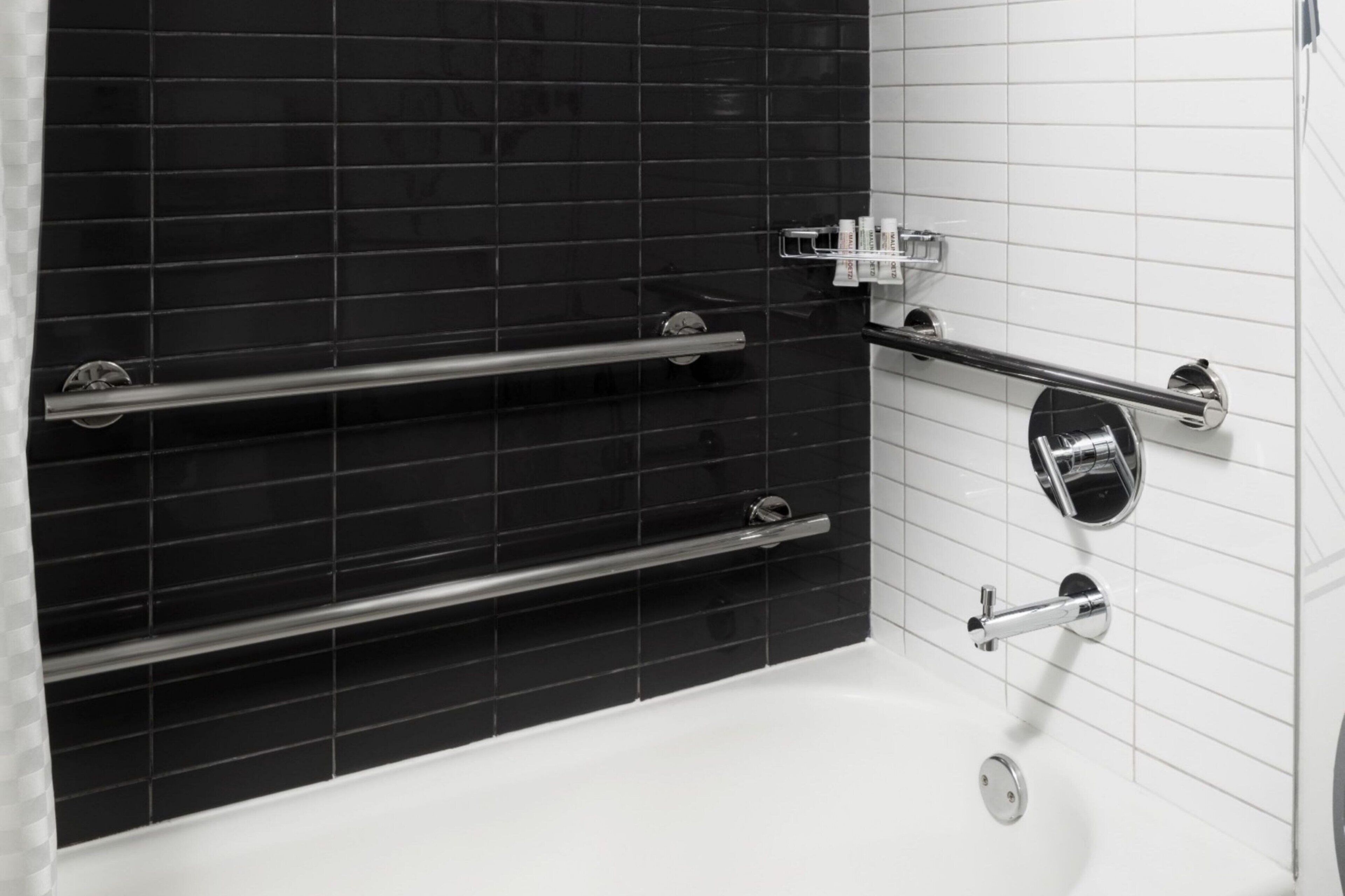 Ein Badezimmer mit schwarzem Fliesenbelag, einer weißen Badewanne und chromfarbenen Armaturen.
