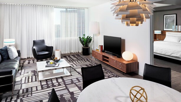 A modern hotel room with a large bed, a flat-screen TV, a dining table, a sofa, and a coffee table. - Le Méridien Chicago - Oakbrook Center (Oak Brook)
