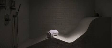 A dimly lit bathroom with a curved shower wall, a towel hanging on the wall, and a bathtub.