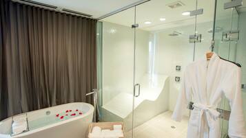 Un baño moderno con una bañera independiente, ducha con cerramiento de vidrio y una bata colgada en un perchero.