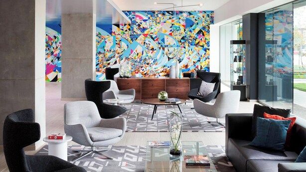 A modern lobby with contemporary furniture, a large abstract mural, and a glass coffee table. - Le Méridien Chicago - Oakbrook Center (Oak Brook)