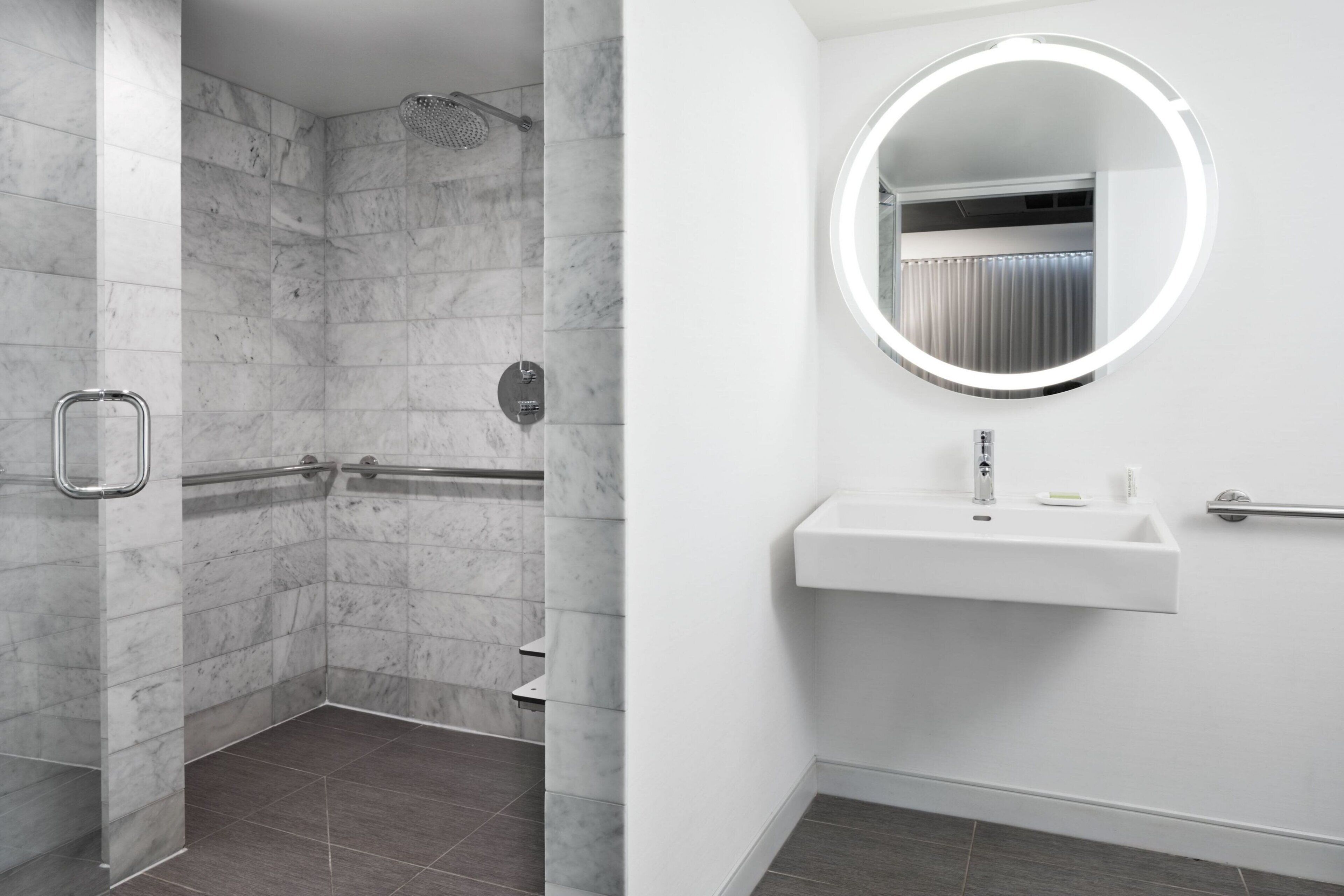Ein modernes Badezimmer mit begehbarer Dusche, einem weißen Waschbecken mit Spiegel und einer Haltestange.