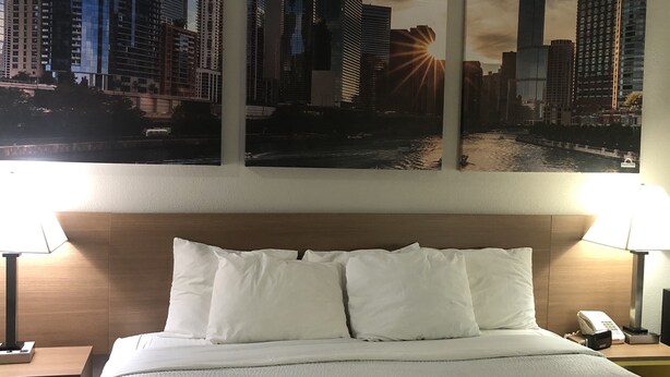 Una habitación de hotel con una cama, dos lámparas de noche y tres cuadros con vistas urbanas en la pared.