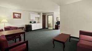 Habitación de hotel con una mesa de comedor, dos sillas, una mesita de centro, una kitchenette, un televisor y un cuadro en la pared.