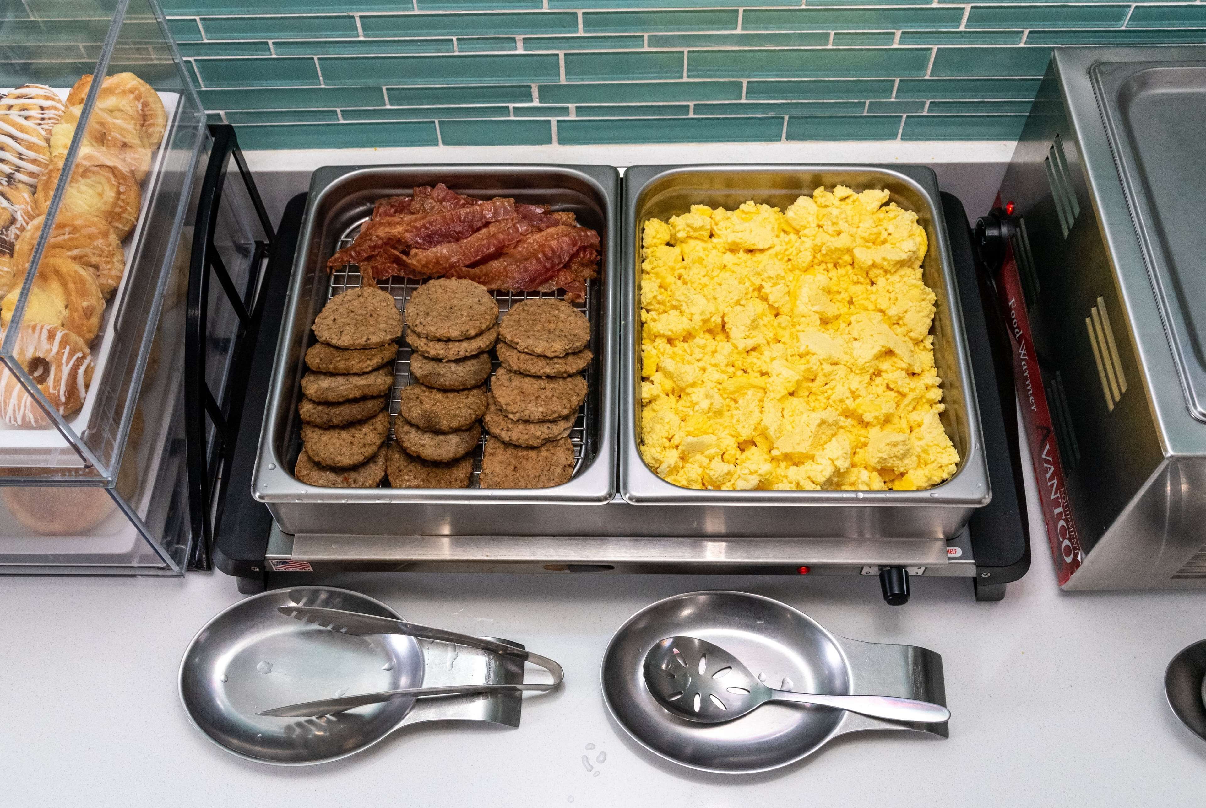 A breakfast buffet with trays of cookies, bacon, and scrambled eggs.