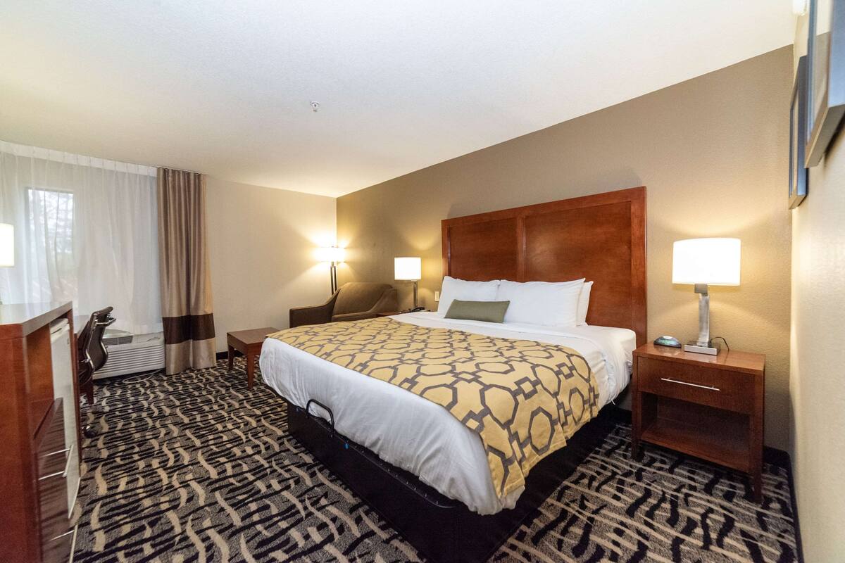 A hotel room with a large bed, two bedside tables with lamps, a desk with a chair, and a patterned carpet.