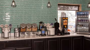 Una cocina con salpicadero de azulejos verdes, una cafetera, un hervidor y un refrigerador.