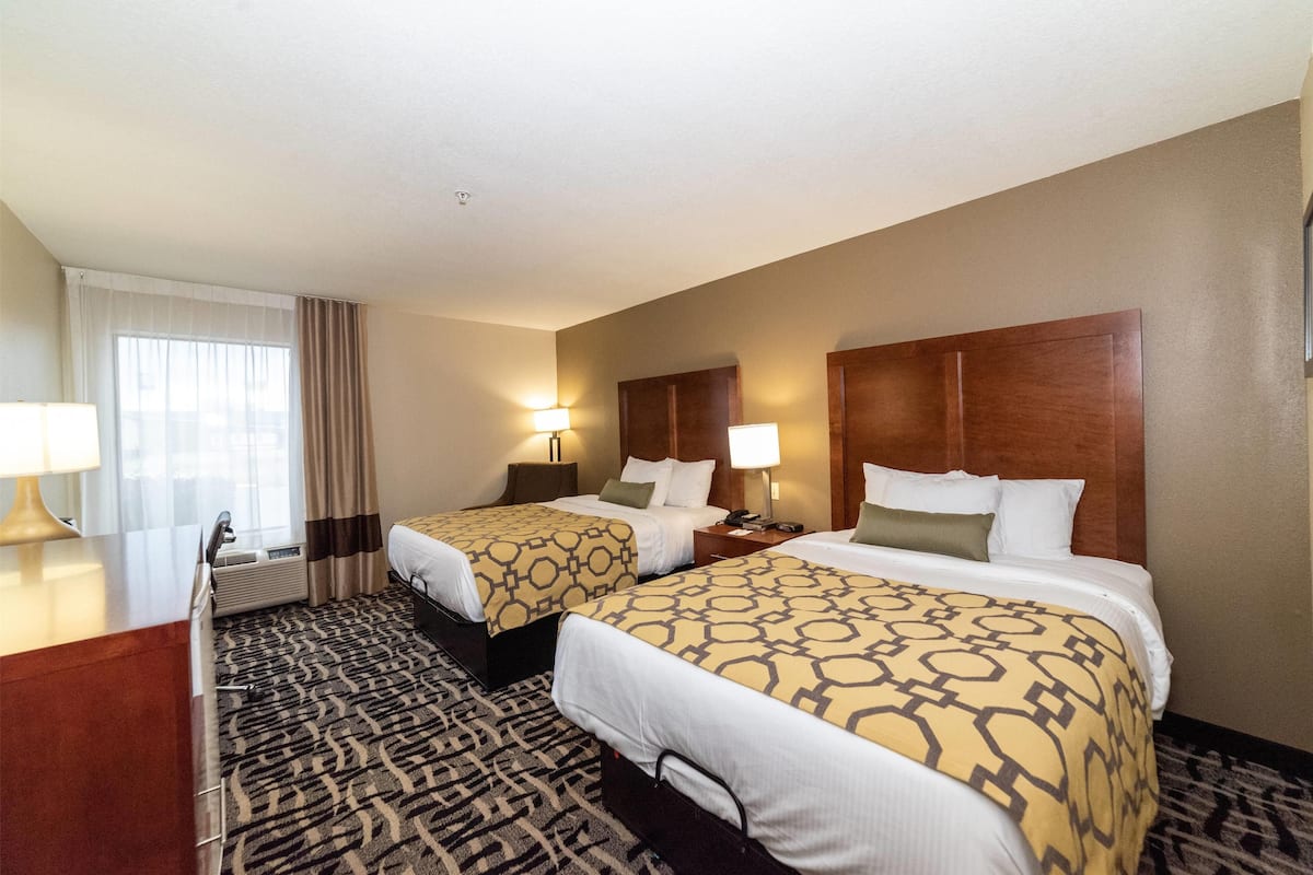 A hotel room with two beds, a desk, a chair, a lamp, and a window with curtains.