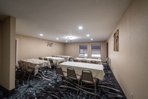 Un salón de conferencias con varias mesas y sillas, paredes color beige y una alfombra estampada.