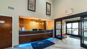 Ein Hotel-Empfangsbereich mit einem Holzbüro, einem blauen Teppich mit dem Hotelnamen und einem Hinweisschild über der Tür.