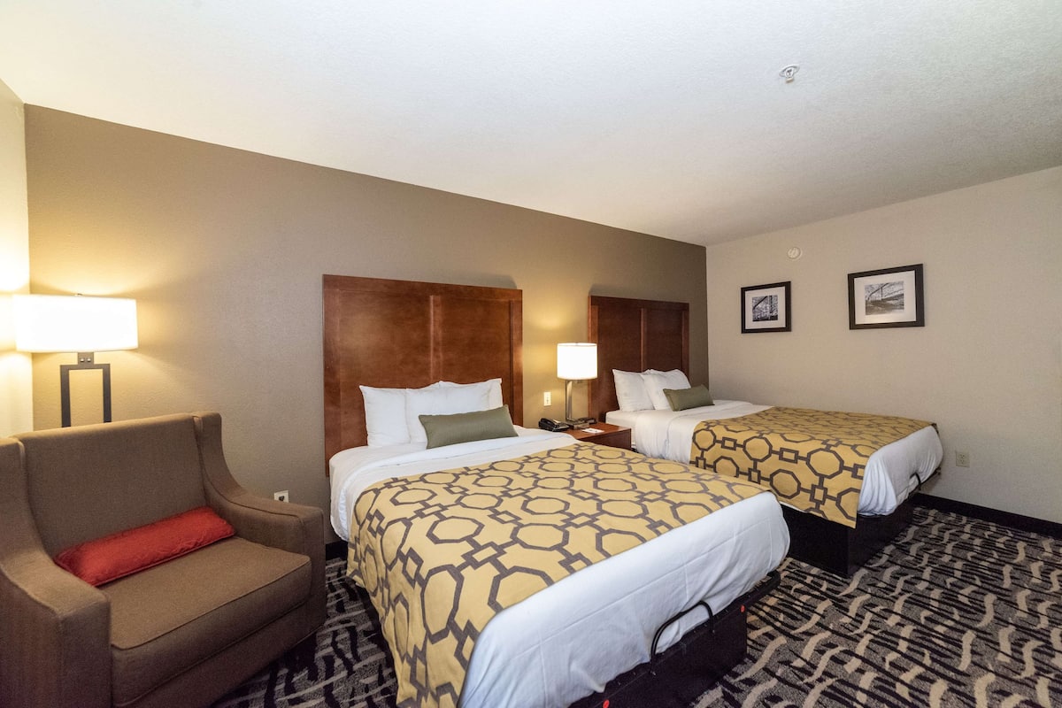 A hotel room with two beds, a sofa, and a nightstand with lamps.