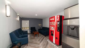 A modern living room with a sofa, chairs, a glass coffee table, a red Coca-Cola vending machine, and a refrigerator.