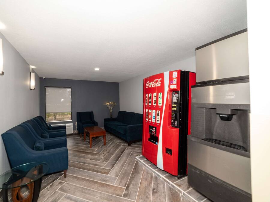 A modern living room with a sofa, chairs, a glass coffee table, a red Coca-Cola vending machine, and a refrigerator.