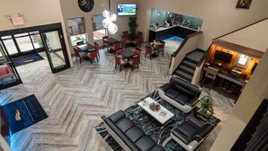 Eine Hotelhalle mit Fischgrätparkett, einer Sitzecke mit schwarzen Ledersofas, einer Bar mit Fernseher und einer Treppe zu einer oberen Ebene.