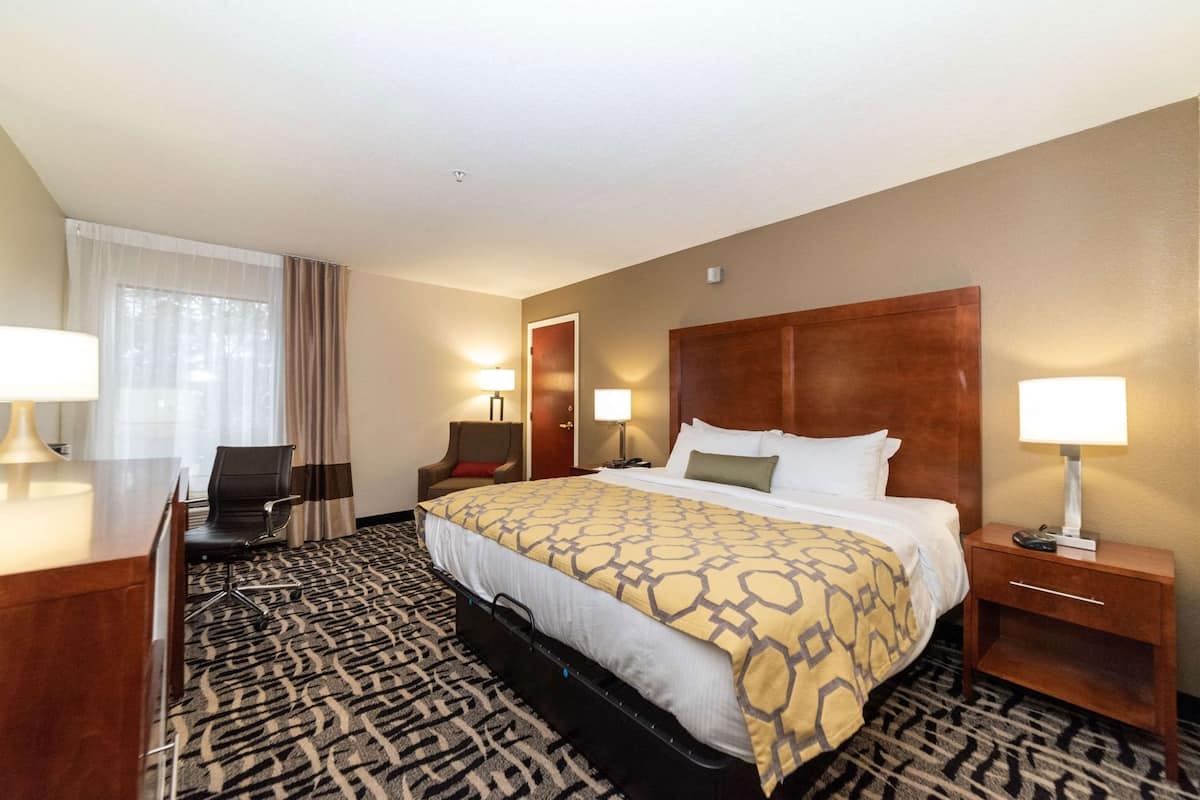 A hotel room with a large bed, a desk, a chair, a nightstand, and a window with curtains.