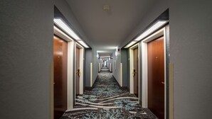Ein Hotelkorridor mit einem gemusterten Teppich, Türen auf beiden Seiten und Deckenbeleuchtung.