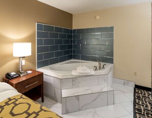 Un baño de hotel con una bañera grande, una mesita de noche con lámpara y un teléfono.