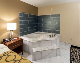 Un baño de hotel con una bañera grande, una mesita de noche con lámpara y un teléfono.
