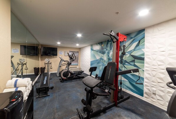 Un gimnasio con equipo de ejercicio, una banca y un televisor en la pared.