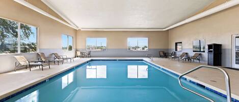 An indoor swimming pool with clear blue water, surrounded by lounge chairs and a tiled deck.