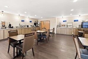 A clean, modern restaurant with wooden tables and chairs, a counter with a coffee machine, and a television screen displaying a menu.