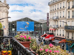 Un hôtel avec une grande enseigne bien visible indiquant « NOUVEL HÔTEL », un bâtiment en verre orné d’une grande publicité bleue, et une rue animée par la présence de piétons.