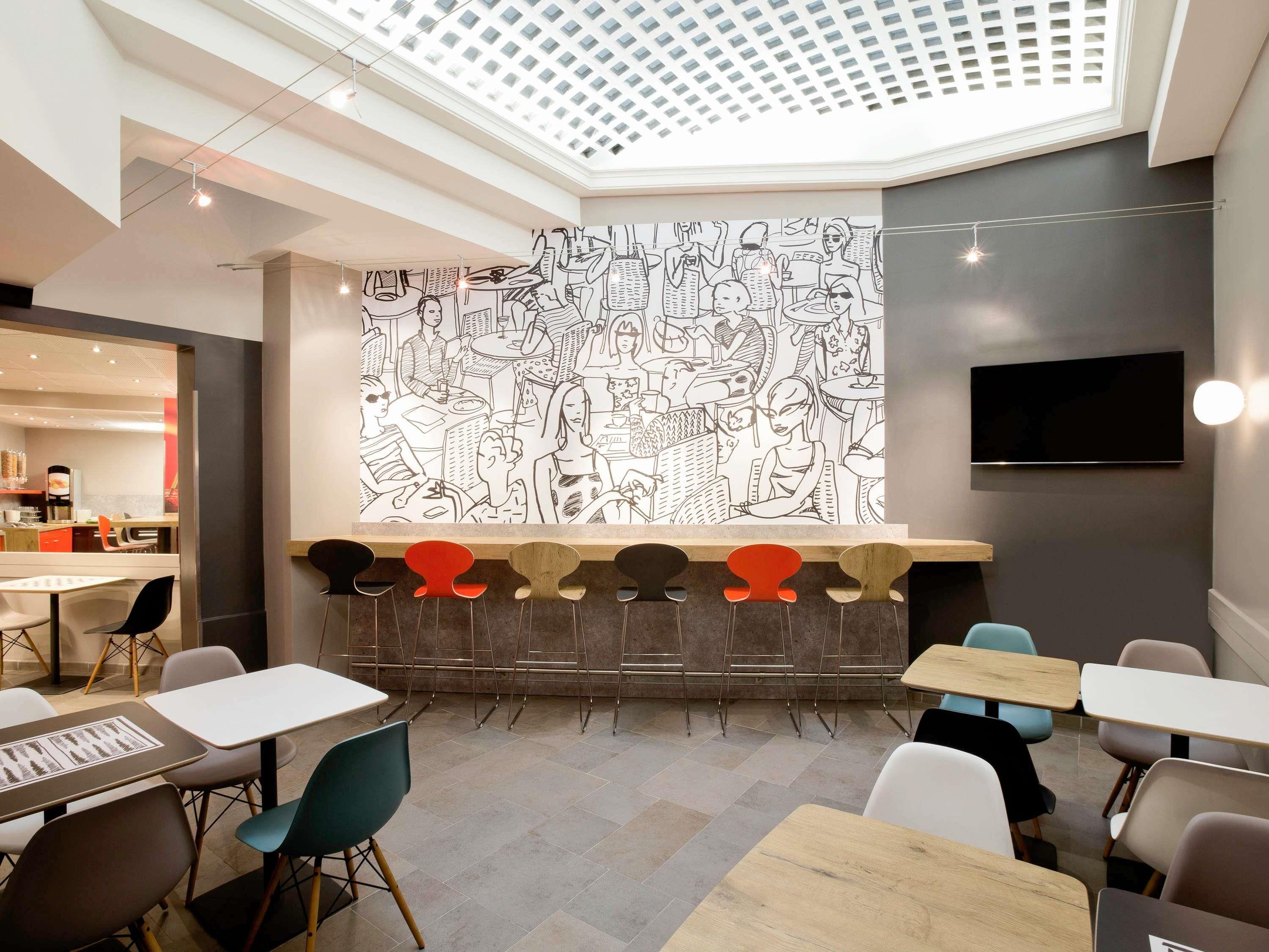 Un interno moderno con soffitto alto, un'area salotto centrale con tavoli e sedie, e un grande affresco a parete.