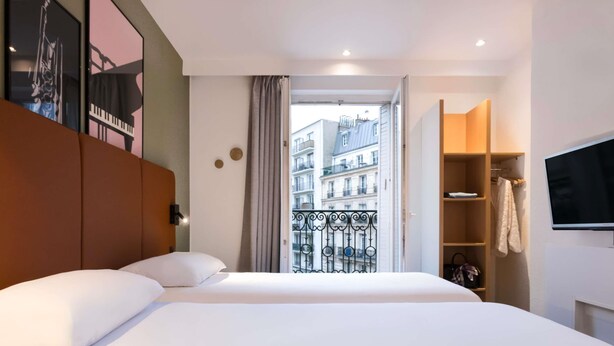 Habitación de hotel con una cama grande, un armario, televisión y un balcón con vistas a edificios.