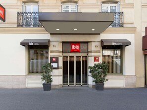 Exterior de um hotel ibis com fachada moderna, portas numeradas e vasos de plantas na entrada.
