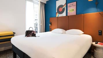 Une chambre d’hôtel avec un grand lit, une valise, un sac à main et une petite table sur laquelle se trouve un livre.