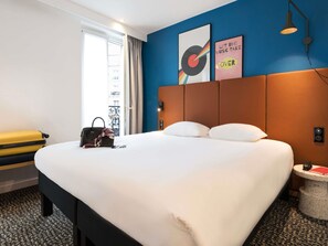Una camera d'albergo con un letto grande, una valigia, una borsa e un tavolino con un libro.