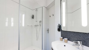 Une salle de bain moderne avec une douche en verre, un lavabo blanc et un miroir avec un pare-éclaboussures noir.