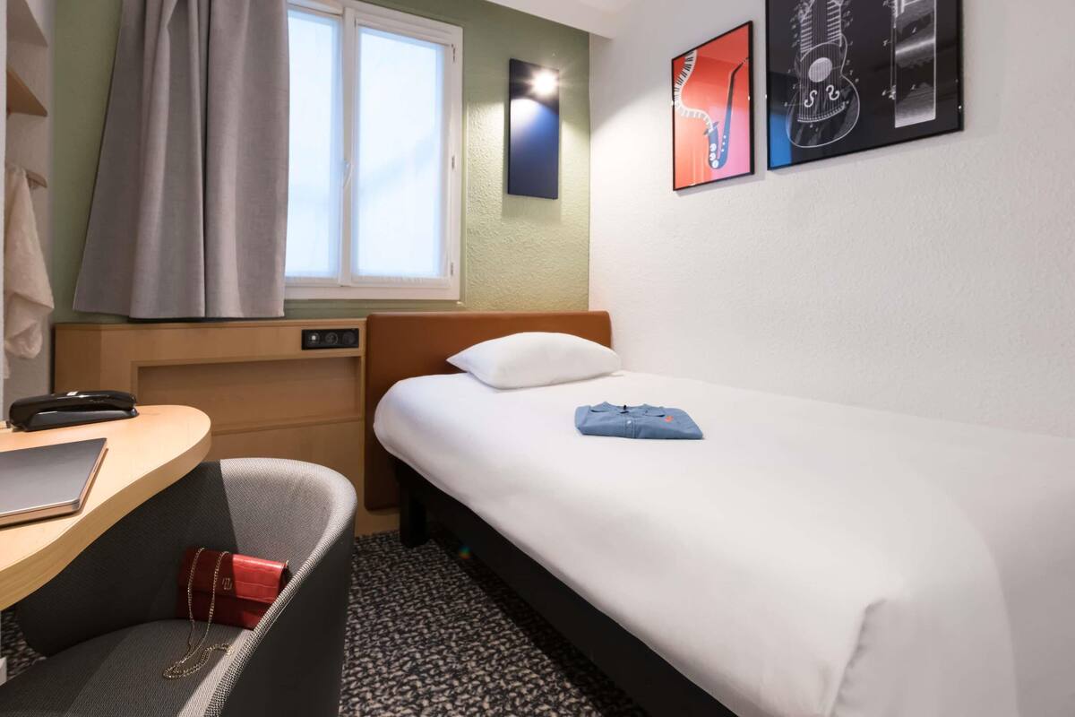 Een hotelkamer met een bed, bureau, stoel, raam met gordijnen en wanddecoratie.