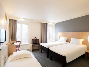 Two single beds with white linens and a flat-screen TV are featured in this stylish room.